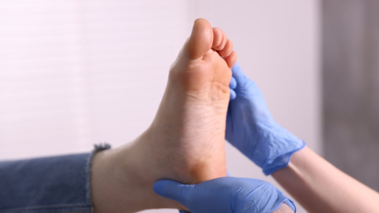 Podiatrist in blue gloves examining the sole of a patient's foot